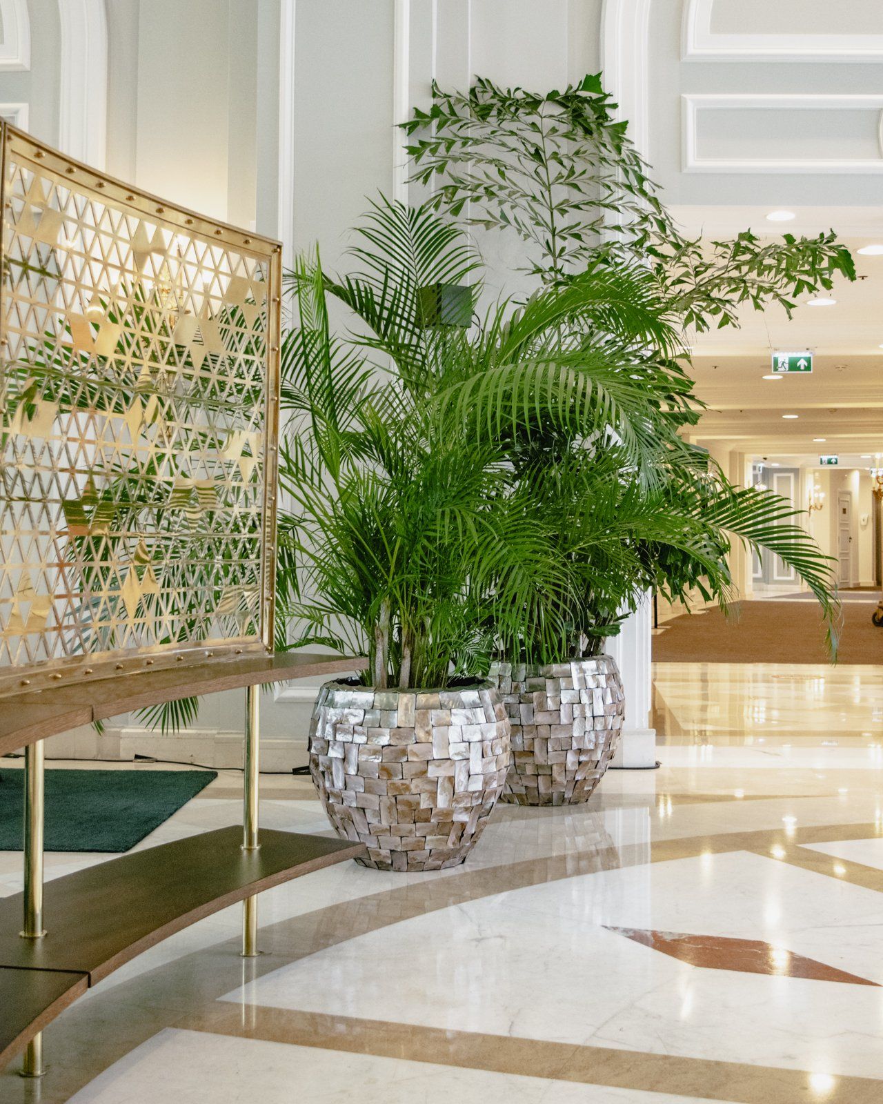 Indoor lobby with large potted palm plants and a patterned bench on a polished floor