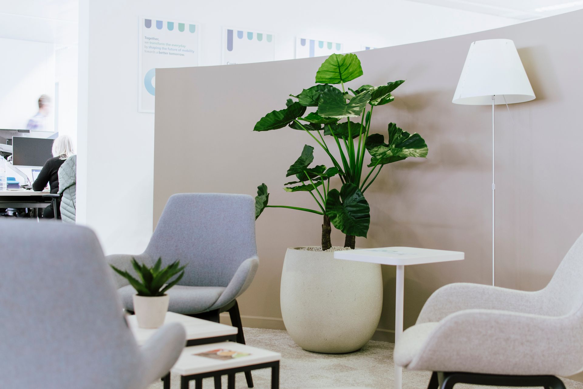 Salle d'attente moderne avec chaises grises, plante en pot et lampadaire blanc