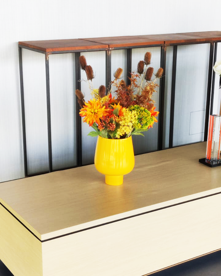 Yellow vase with dried flowers on a wooden cabinet against a white wall