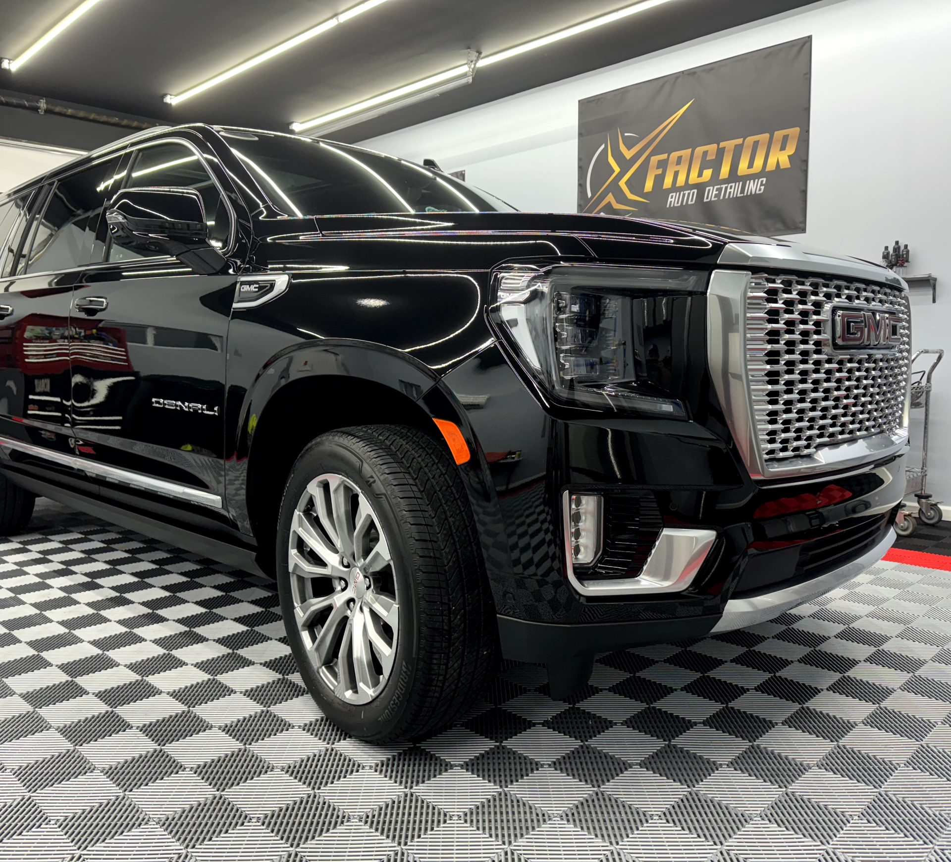 a black gmc yukon is parked in a garage next to a sign that says x factor