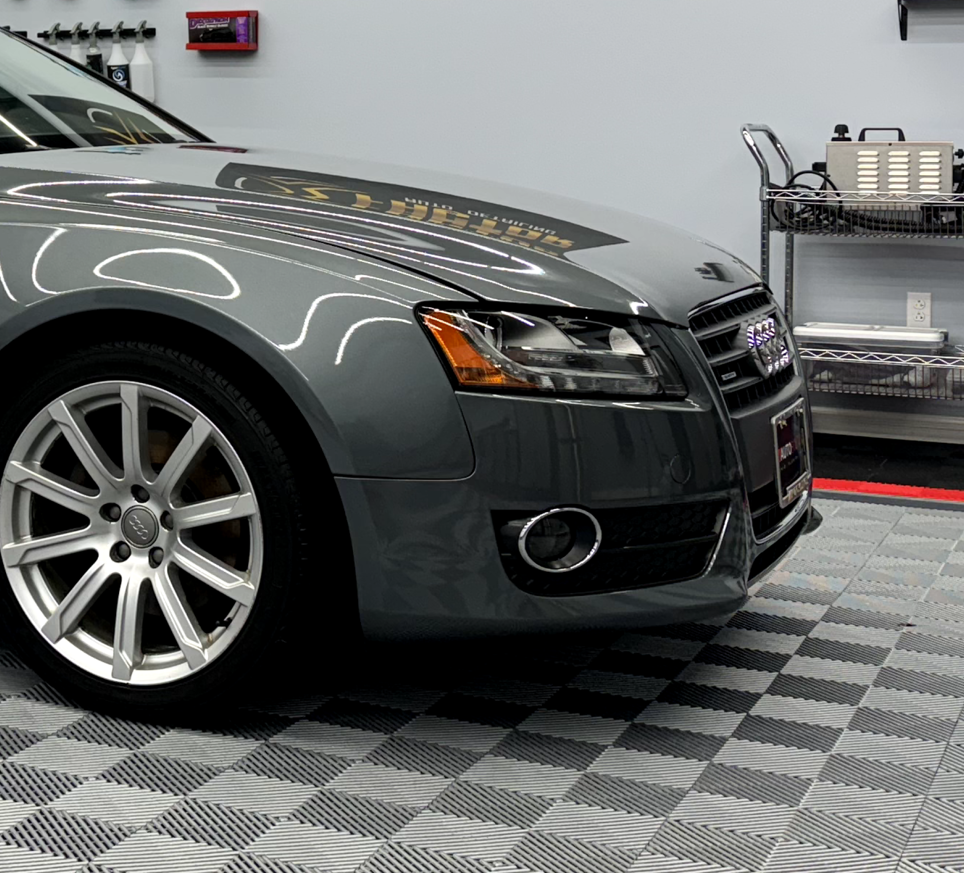 a gray car is parked on a checkered floor in a garage