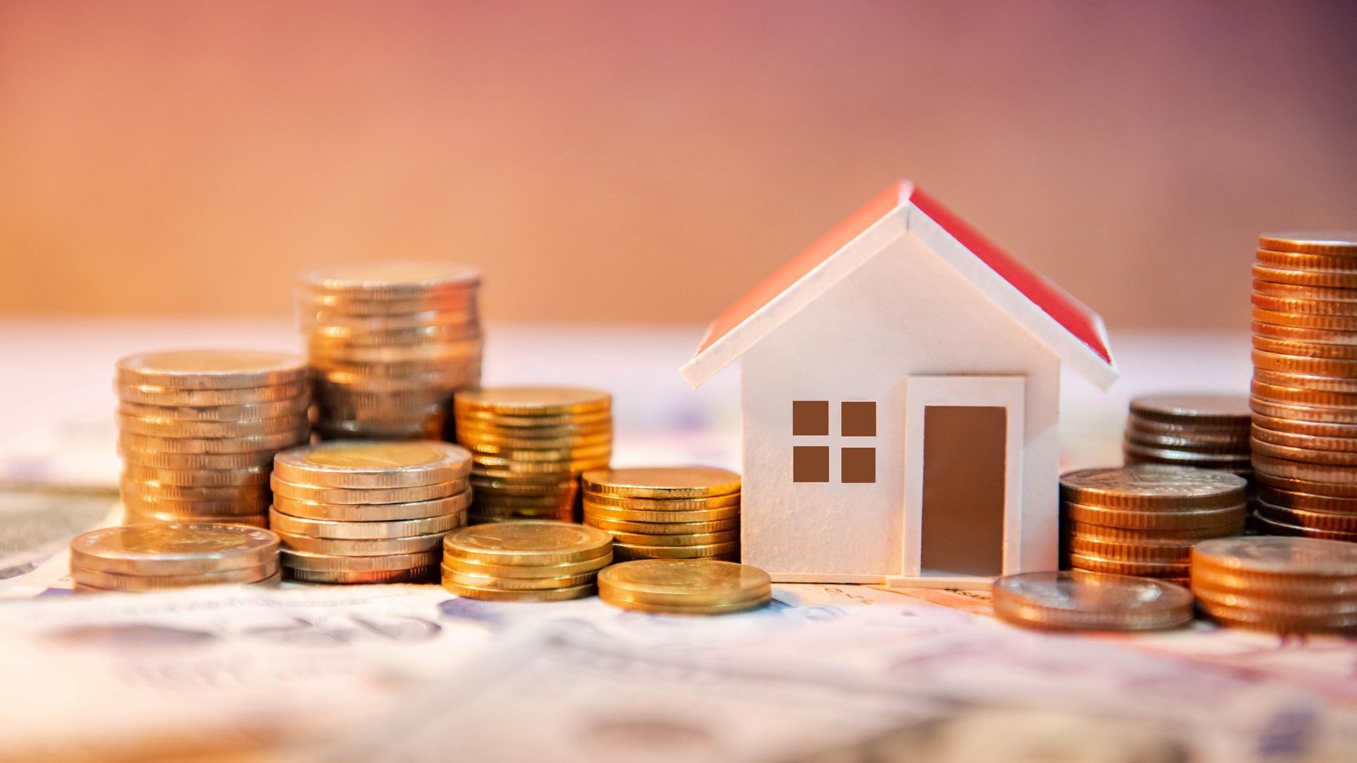 Toy house next to stacks of coins on a blurred background. Financial concept.