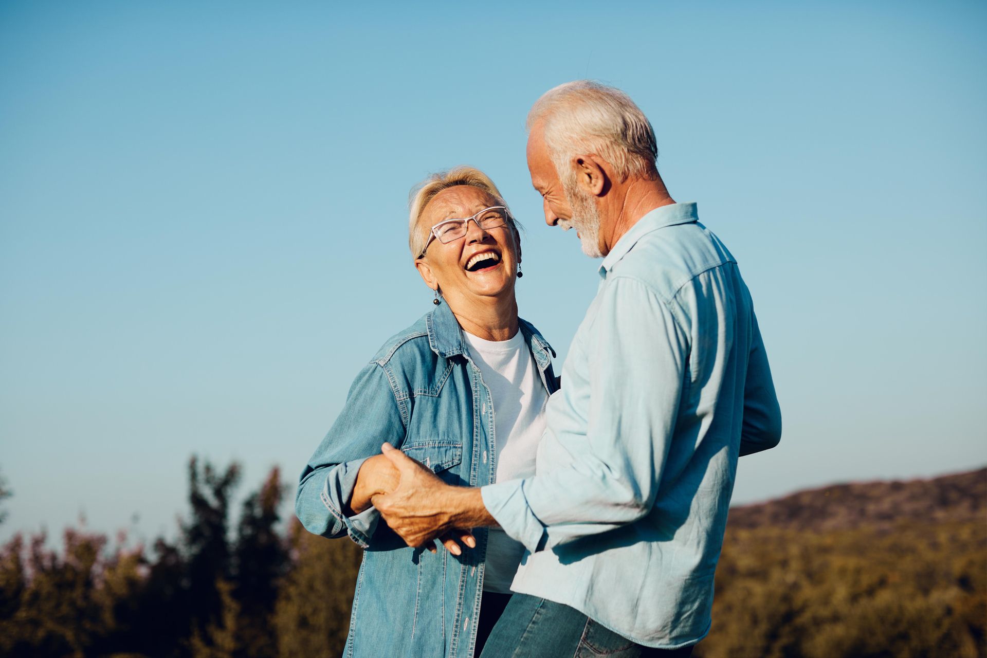 Two people laughing and holding hands outdoors under a clear blue sky