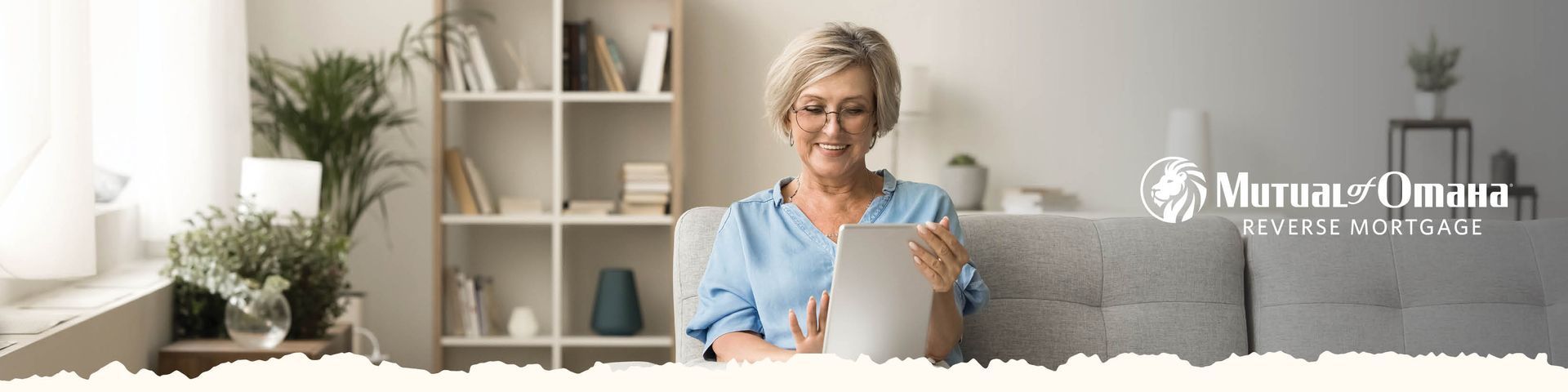 Woman smiling in a bright home office, holding a tablet beside a plant and shelves with a logo on the right
