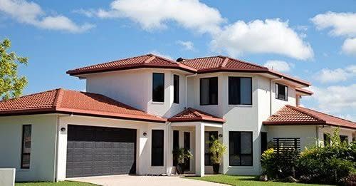 Two-story white house with terracotta roof, black windows, and a dark garage door against a blue sky