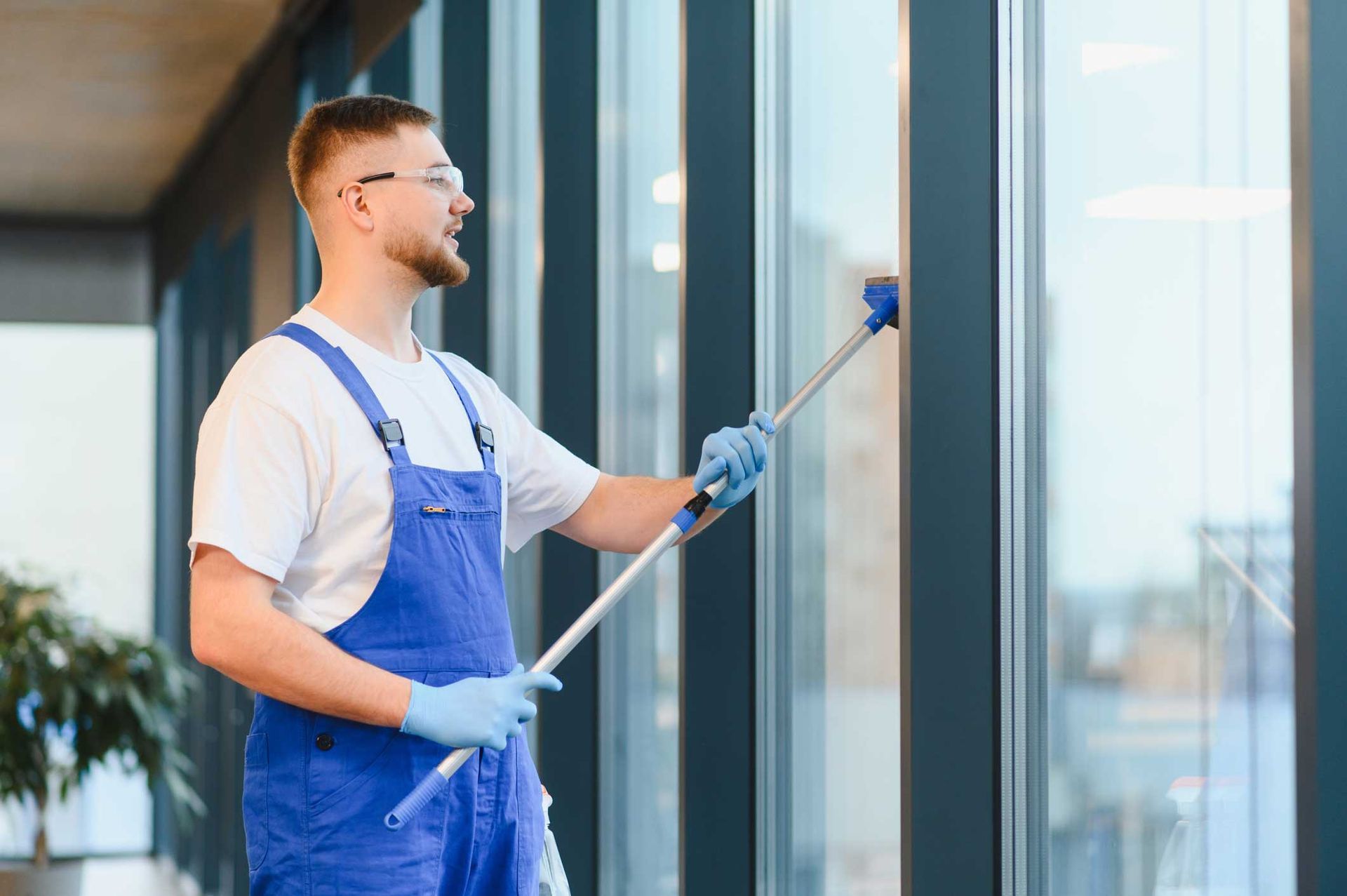Worker in blue overalls cleaning glass windows with a squeegee