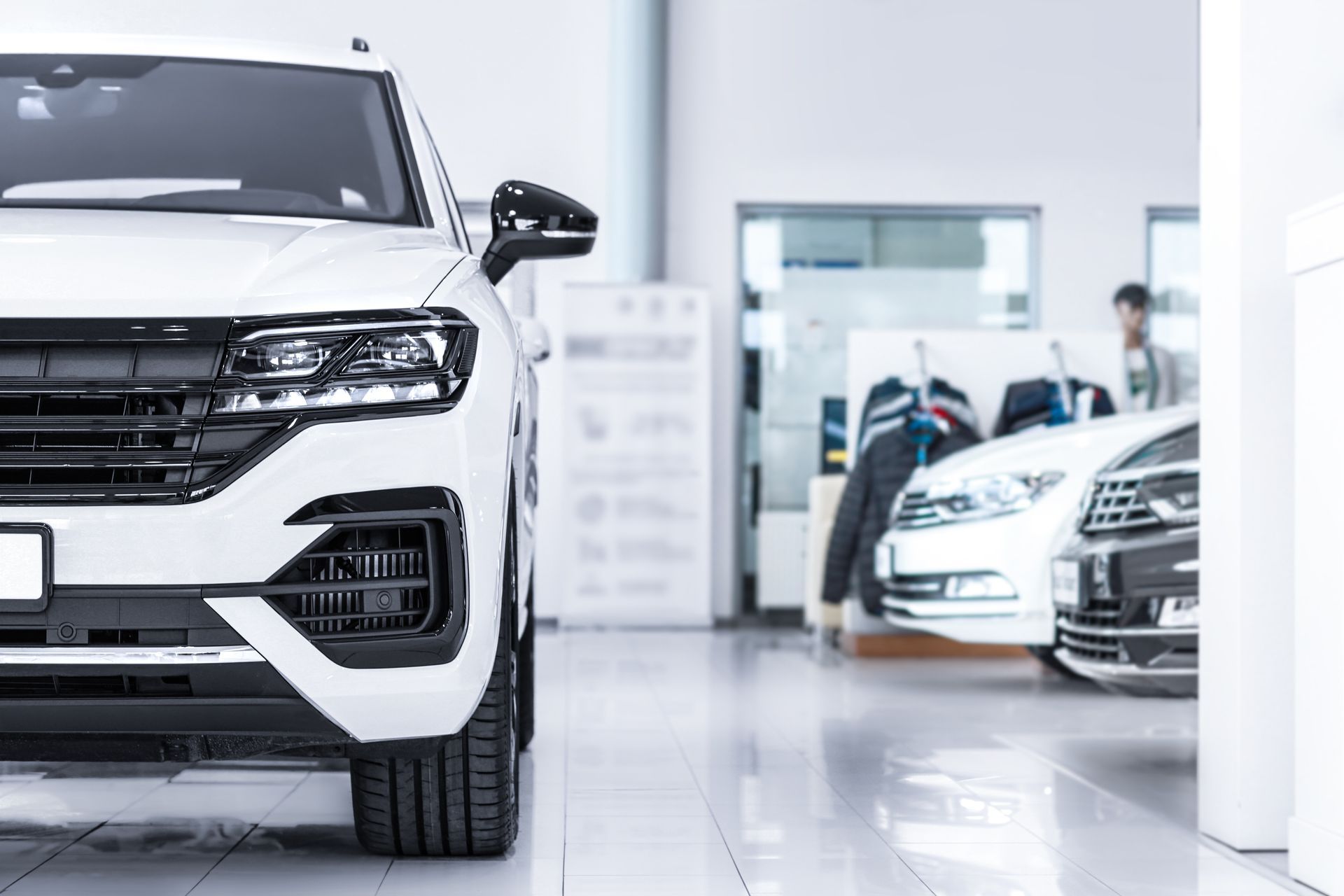White SUV in a bright car showroom, with other cars and staff in the background
