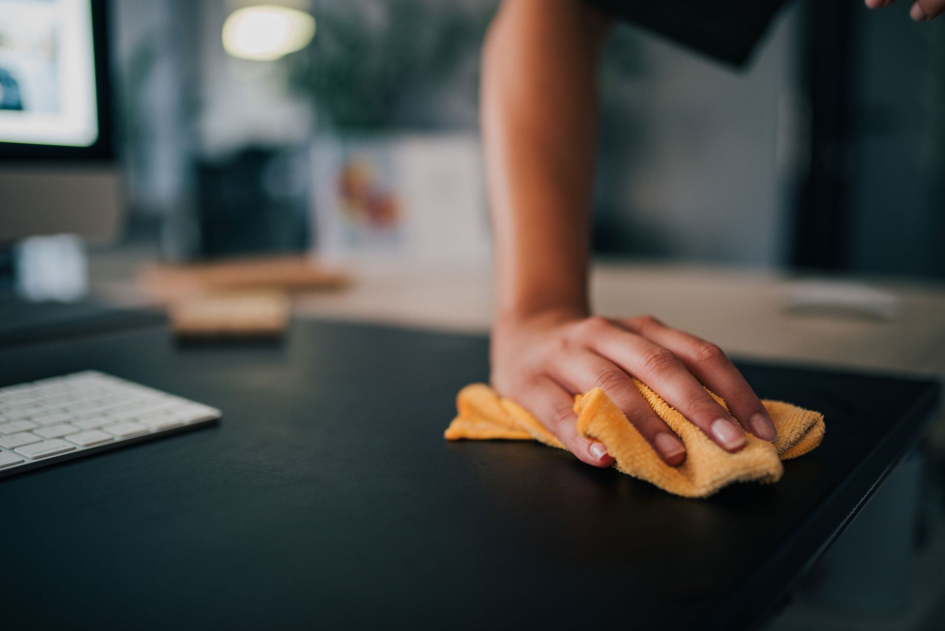 Hand with yellow cloth cleaning a dark desk in an office. Hand with yellow cloth cleaning a dark desk in an office.