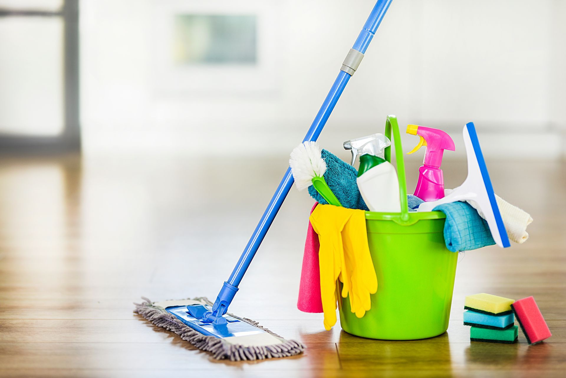 Cleaning supplies in a green bucket with a mop on a wooden floor Cleaning supplies in a green bucket with a mop on a wooden floor
