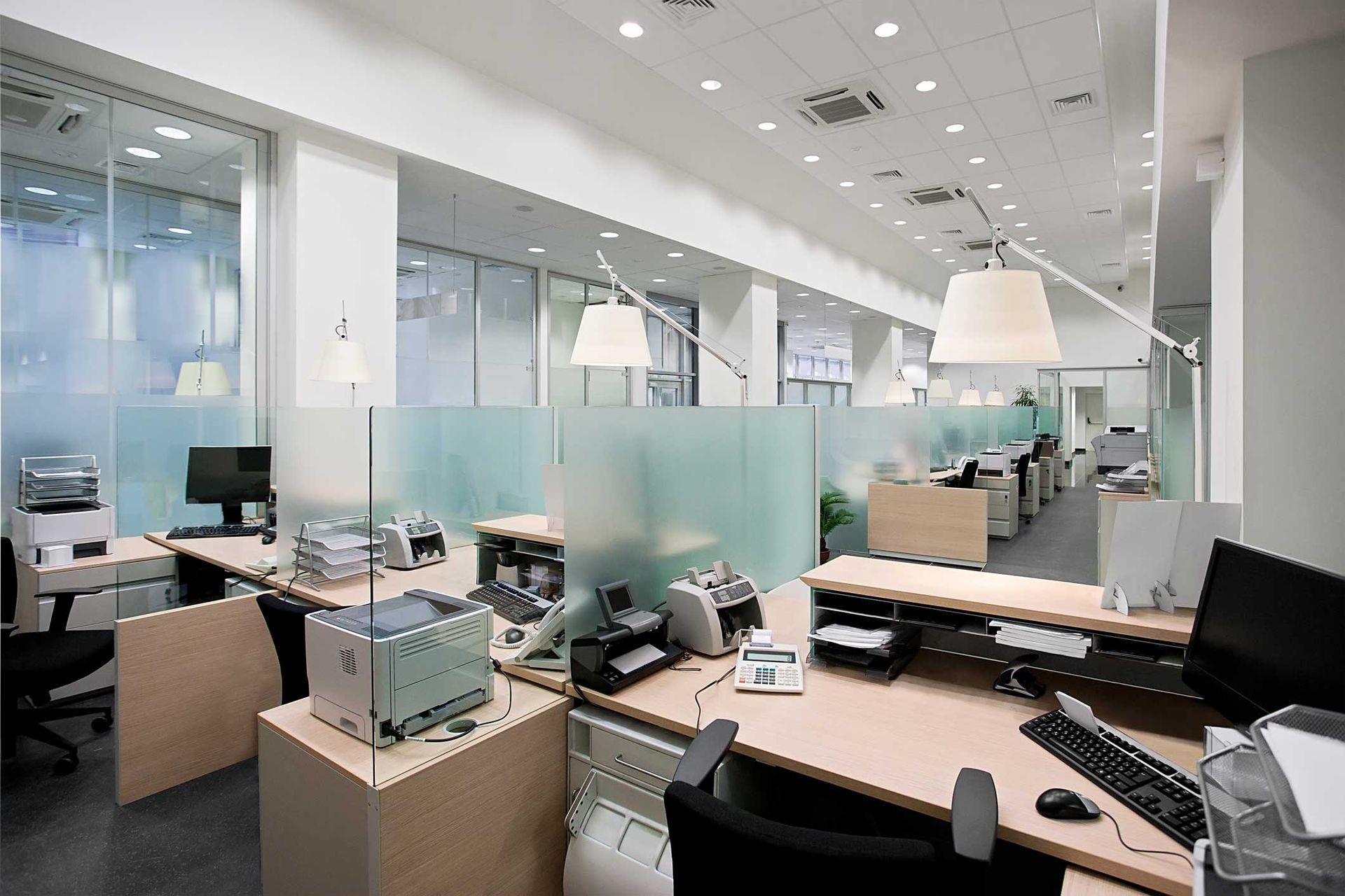 Modern open-plan office with desks, computers, glass partitions, and bright white lighting