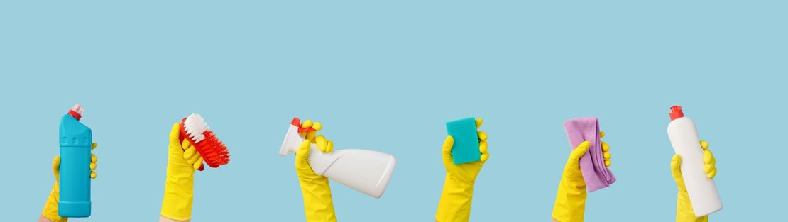 Hands in yellow gloves holding cleaning supplies against a blue background. Hands in yellow gloves holding cleaning supplies against a blue background.