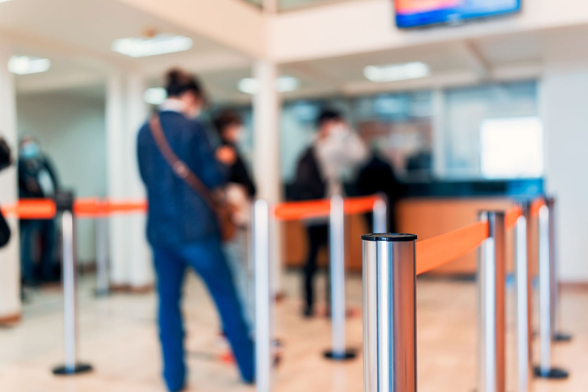 People waiting in line at a bank, roped off with orange barriers.