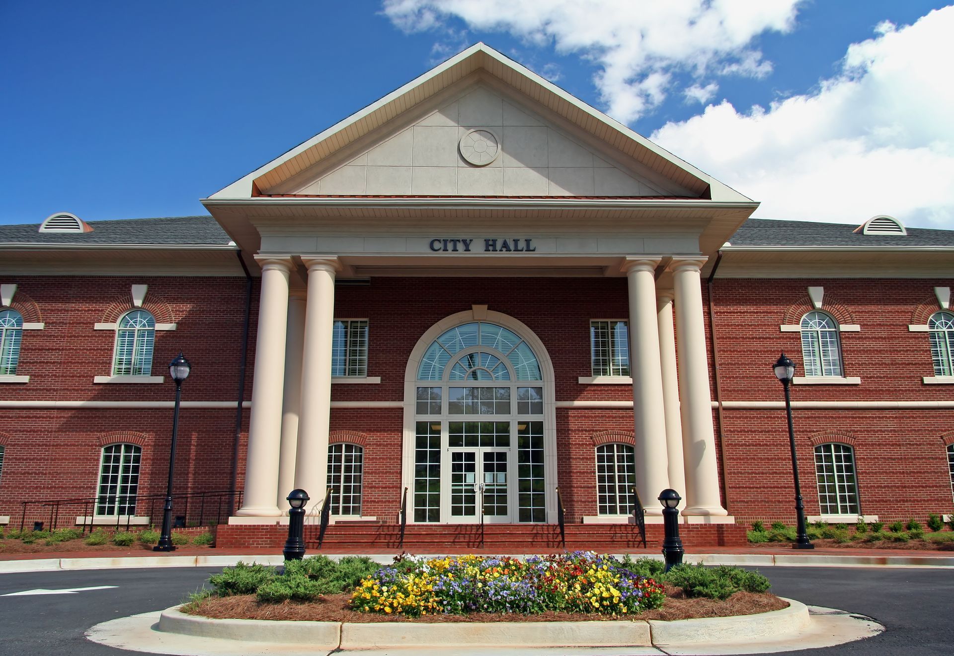 City hall building with red brick, white columns, and a flower bed in front City hall building with red brick, white columns, and a flower bed in front