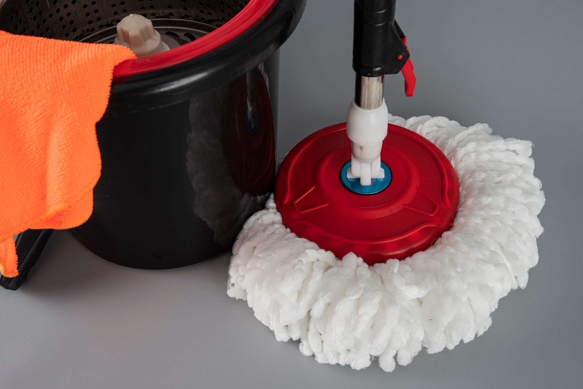 A red-and-white spin mop head beside a black bucket with an orange glove.