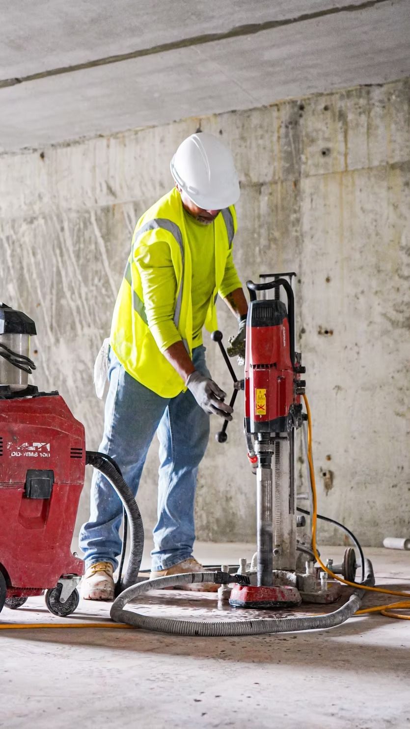 Worker in neon safety jacket and hard hat drilling concrete indoors with a floor saw