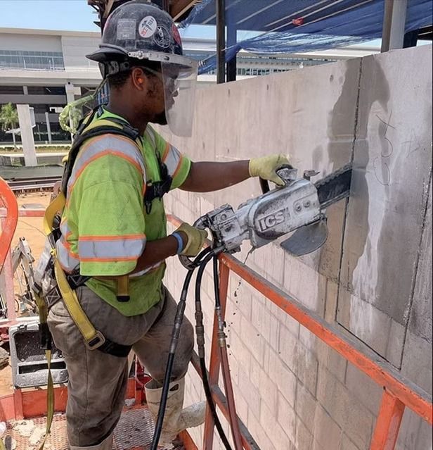 Construction worker cutting a concrete wall with a power saw on a scaffolded job site