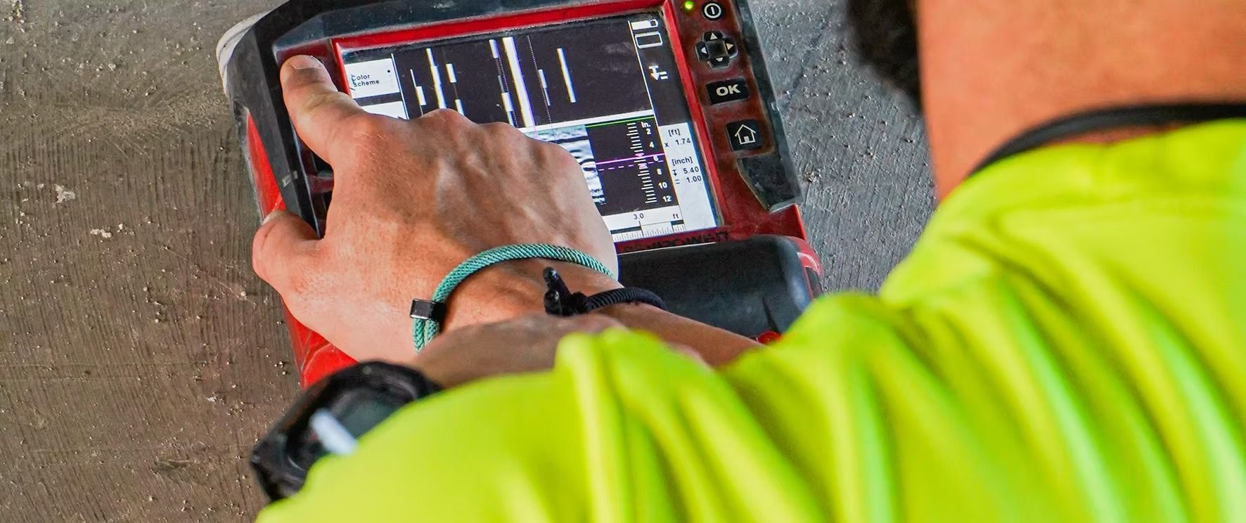 Person holding a red tablet while looking at a screen outdoors, wearing a neon yellow jacket