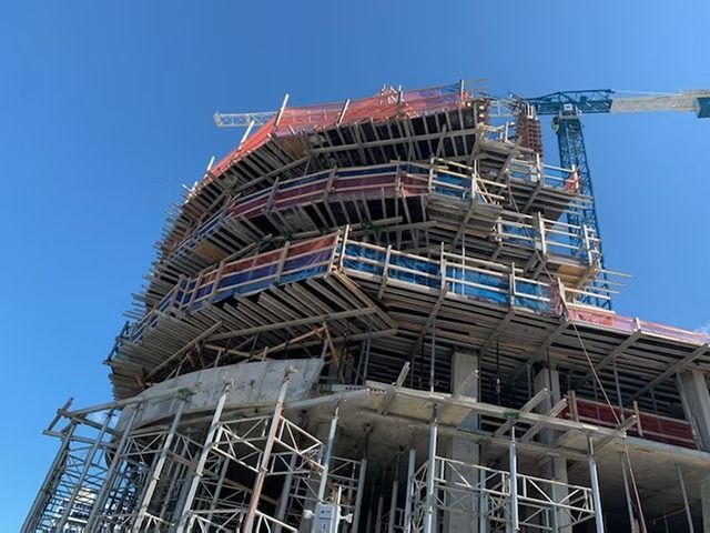 High-rise building under construction with extensive scaffolding against a blue sky