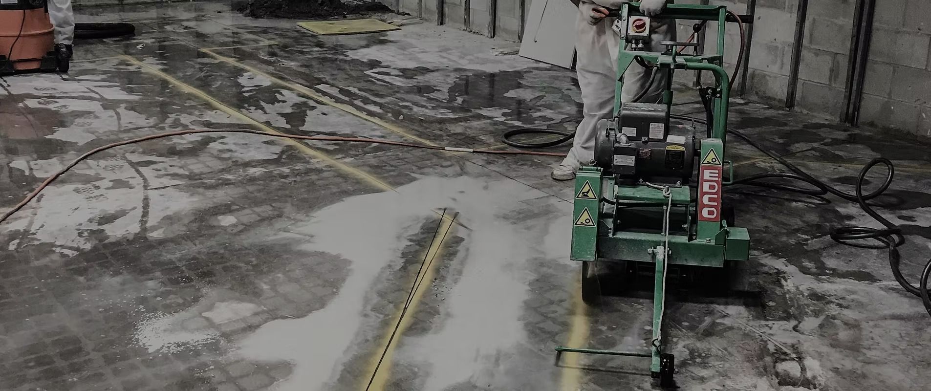 Green industrial machine on a wet concrete floor spraying or cleaning a narrow yellow line.