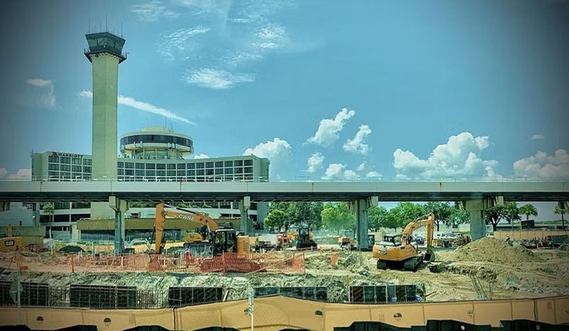 Airport terminal under construction with excavators and a control tower under a blue sky