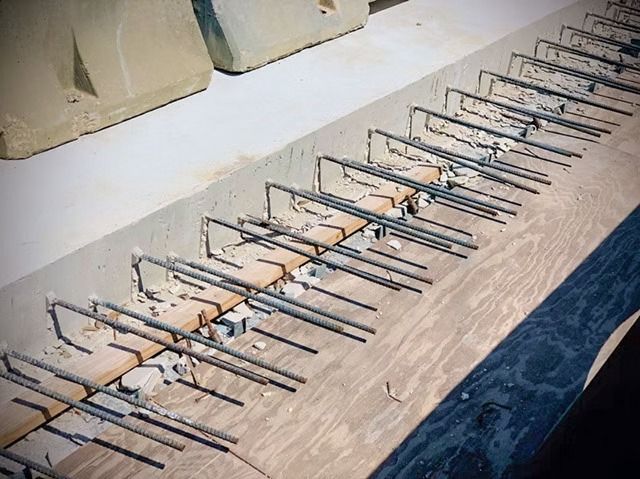 Row of metal rebar tied in triangular frames on a concrete surface, beside a blue tarp edge.