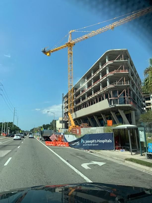 Street view of a modern building under construction beside a road, with a tall yellow crane.