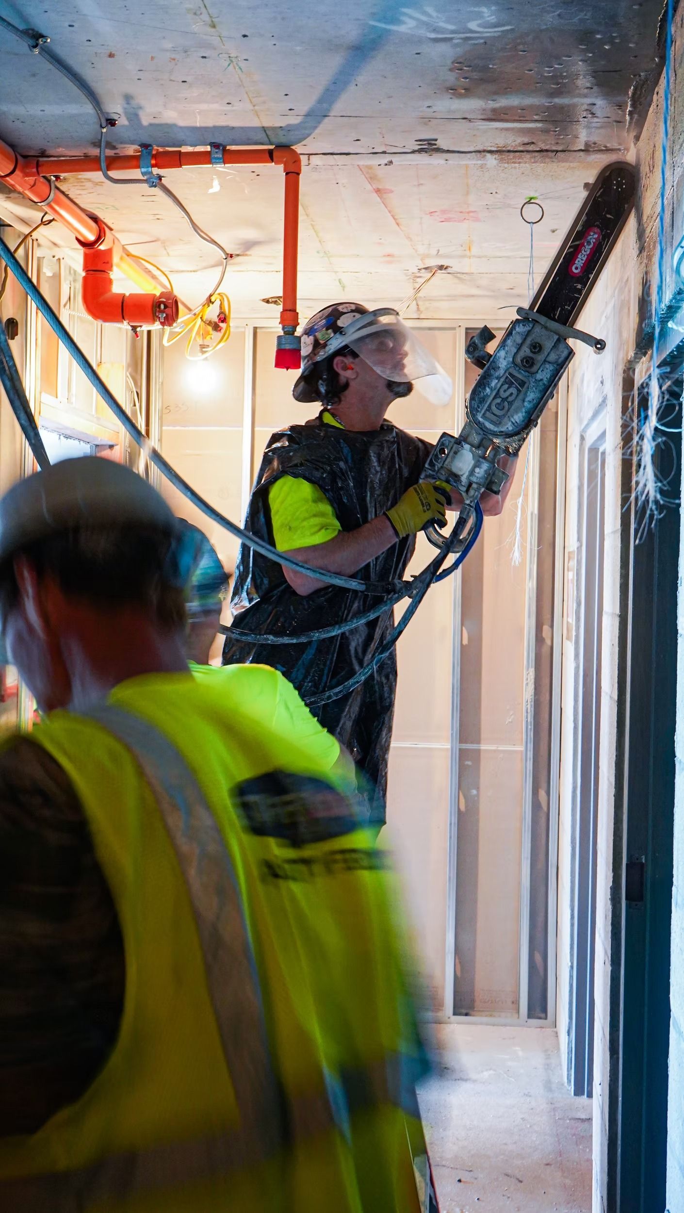 Construction worker sanding a wall with a power tool in a renovation site, wearing a hard hat and safety vest