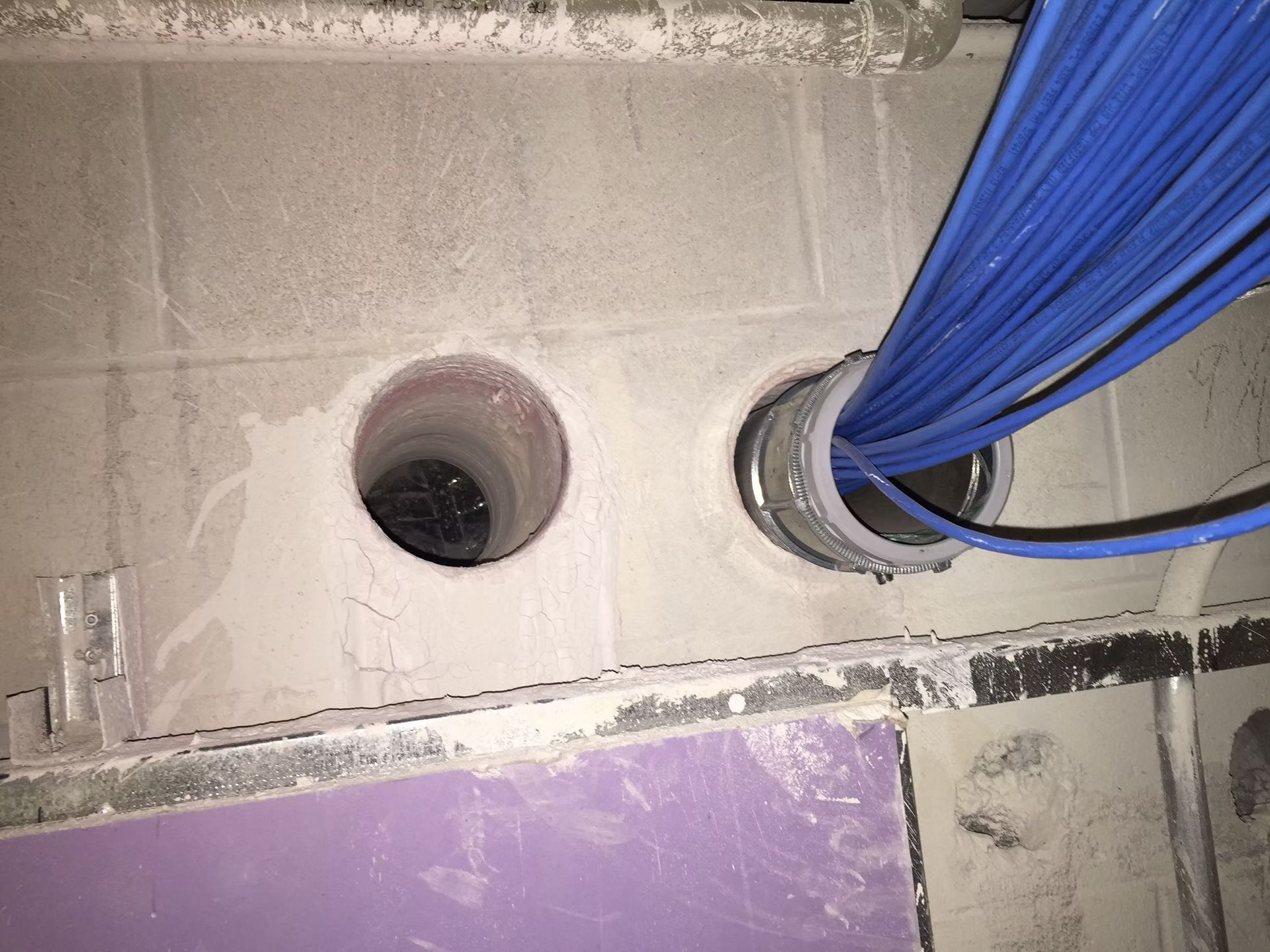 Construction wall with two circular openings, one filled with blue conduit or tarp.