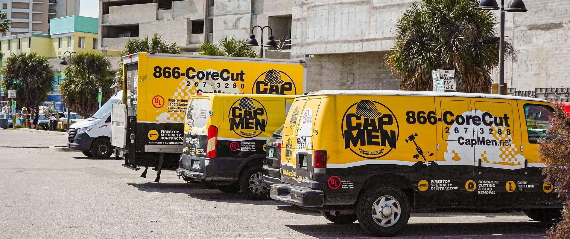 Yellow pest control vans parked on a street beside apartment buildings and a palm tree.