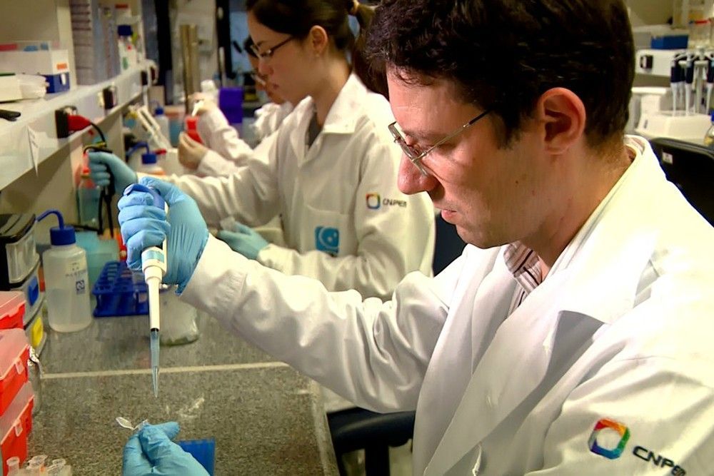 Cientistas de jaleco usando pipetas em uma bancada de laboratório.