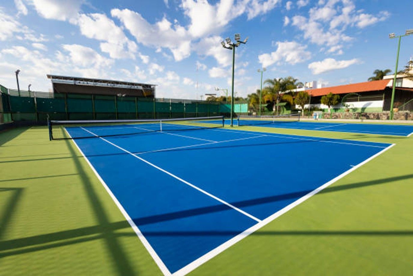 Blue and green outdoor tennis court under a sunny sky