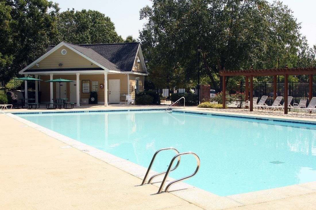 Outdoor swimming pool beside a small building, with blue water and metal ladder under trees