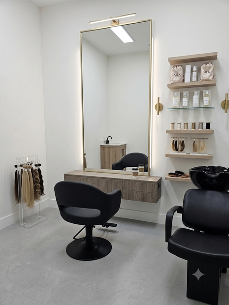 Modern salon interior with two black chairs, wall mirror, shelves, and hair products above a gray floor
