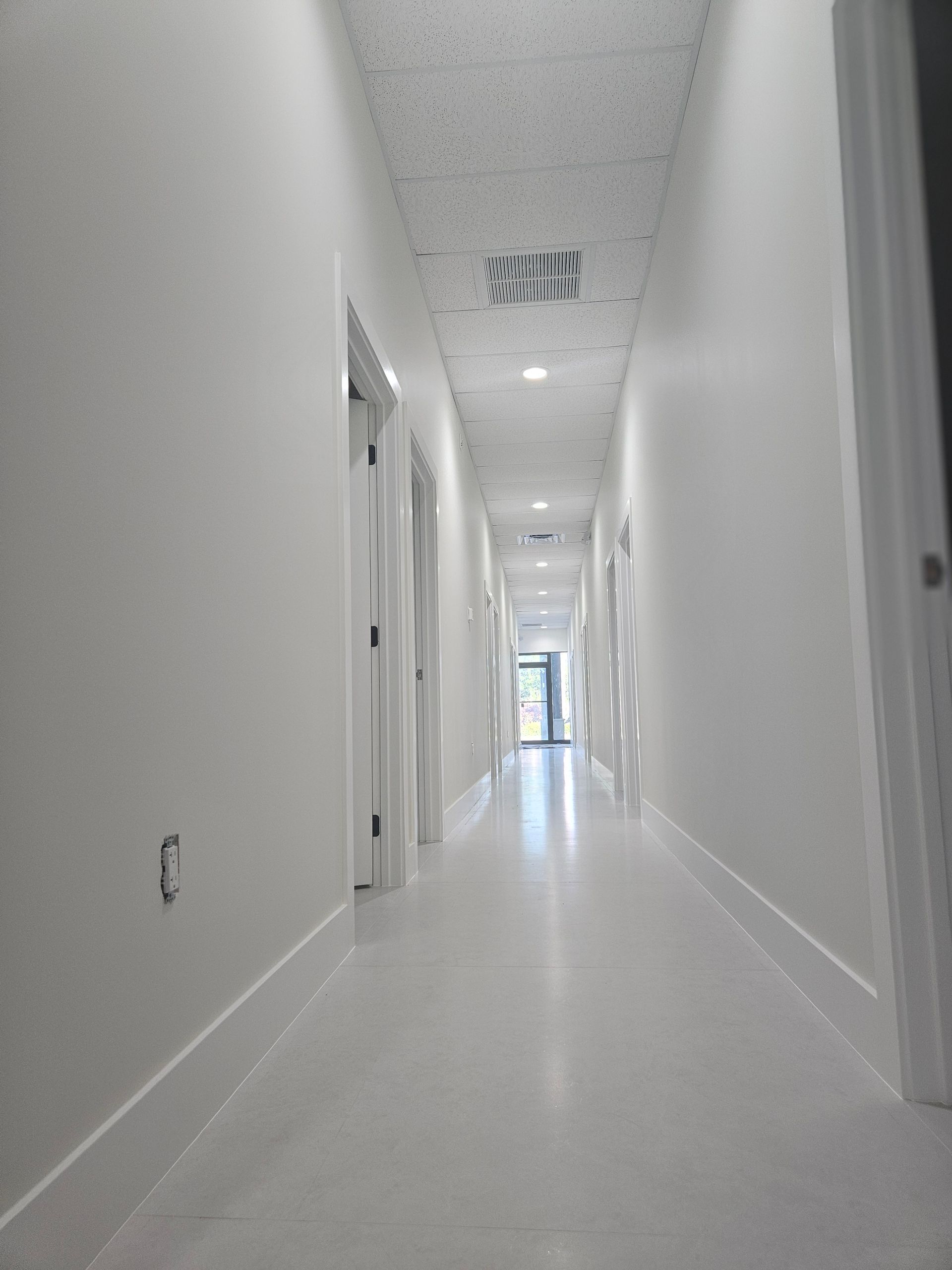 Bright white hallway with doors on both sides and windows at the far end