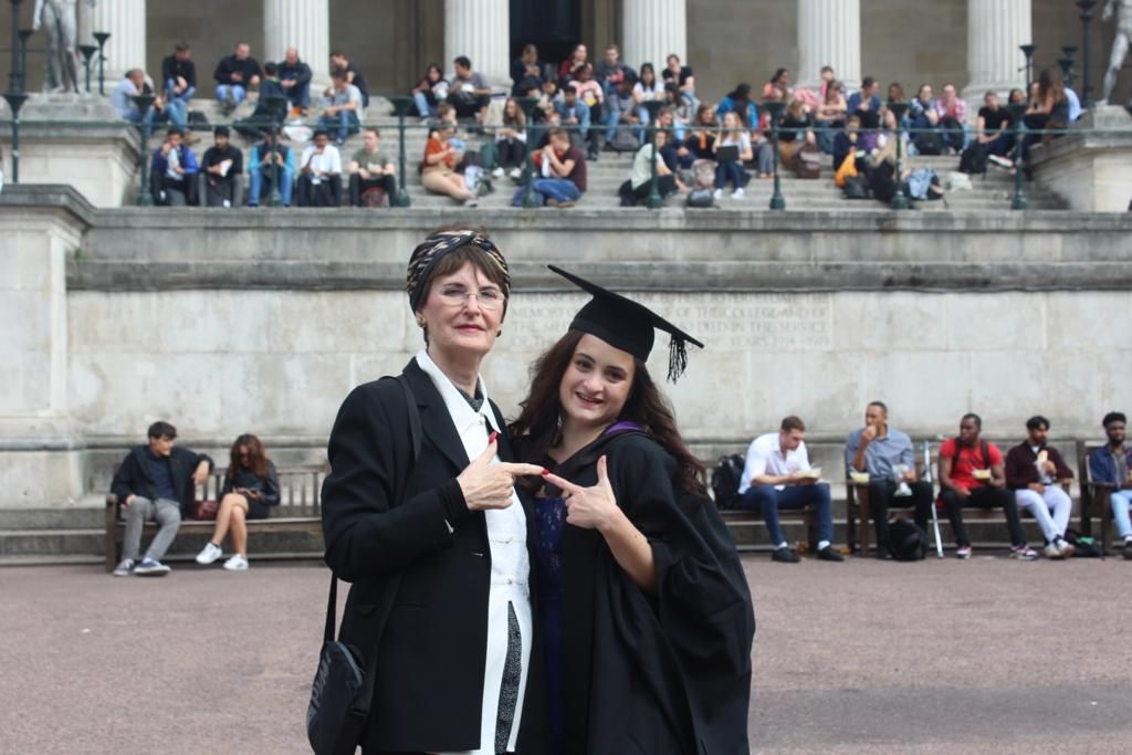 Lauren Lethbridge in a black mortarboard Hat and gown with purple hood. Moira is wearing a black jacket and cream scarf.