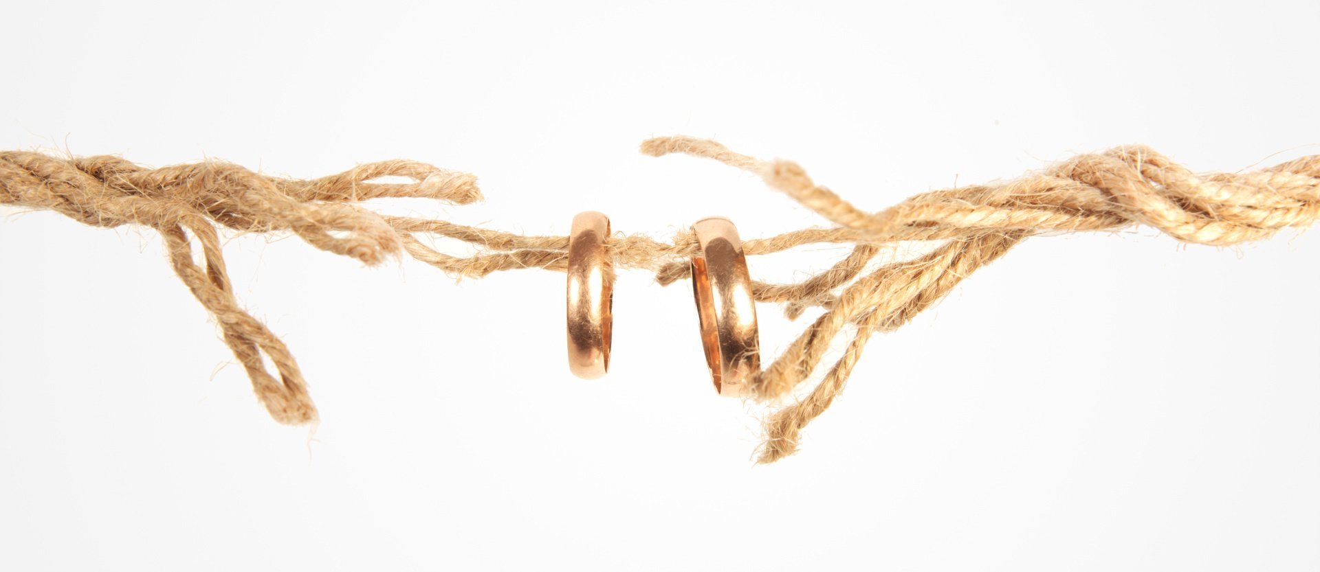 Rope that is frayed one strand holds on two wedding rings.