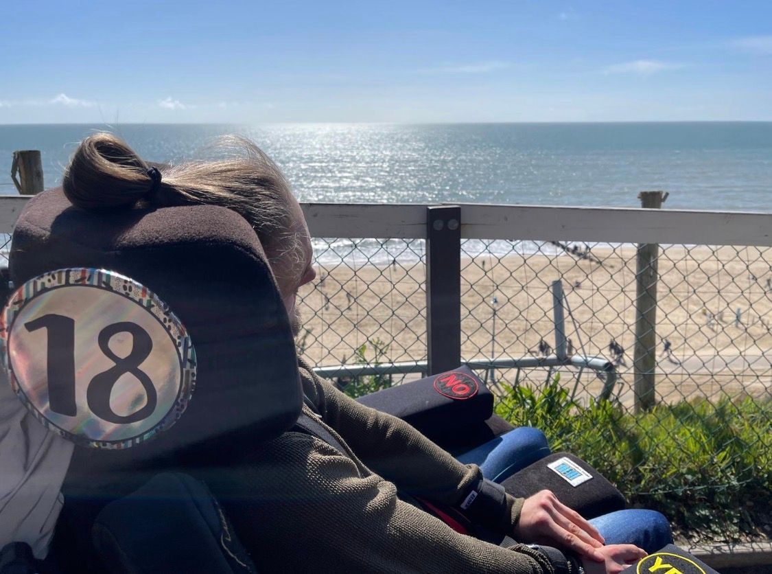 Alfie in his wheelchair with an 18 badge on and overlooking the beach.