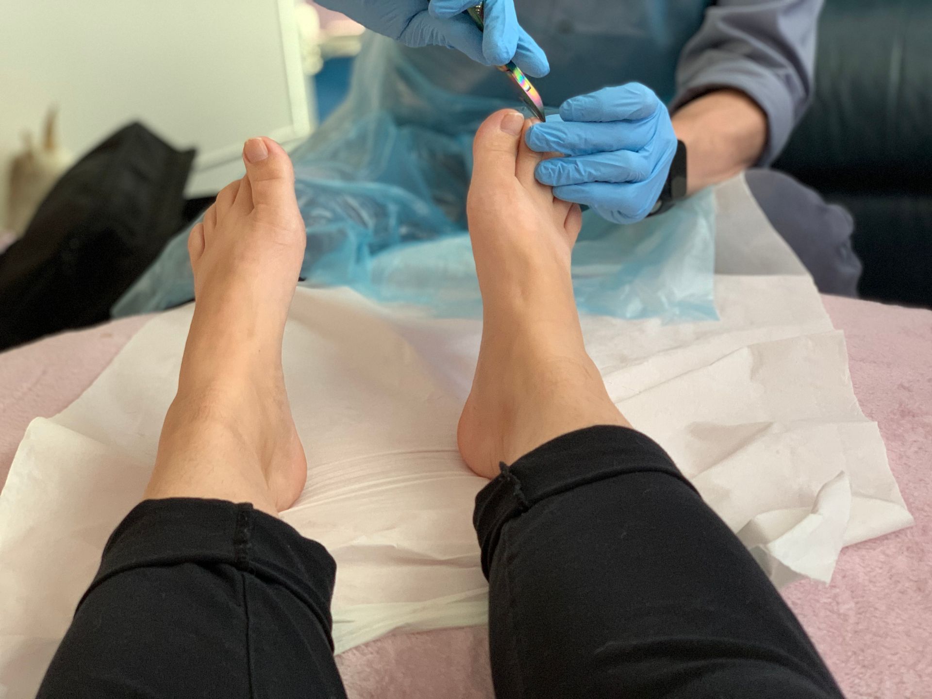 Victoria-Jayne sat in black legging with her feet on paper, hands with blue gloves on and a instrucment in them can be seen being used on the feet. 