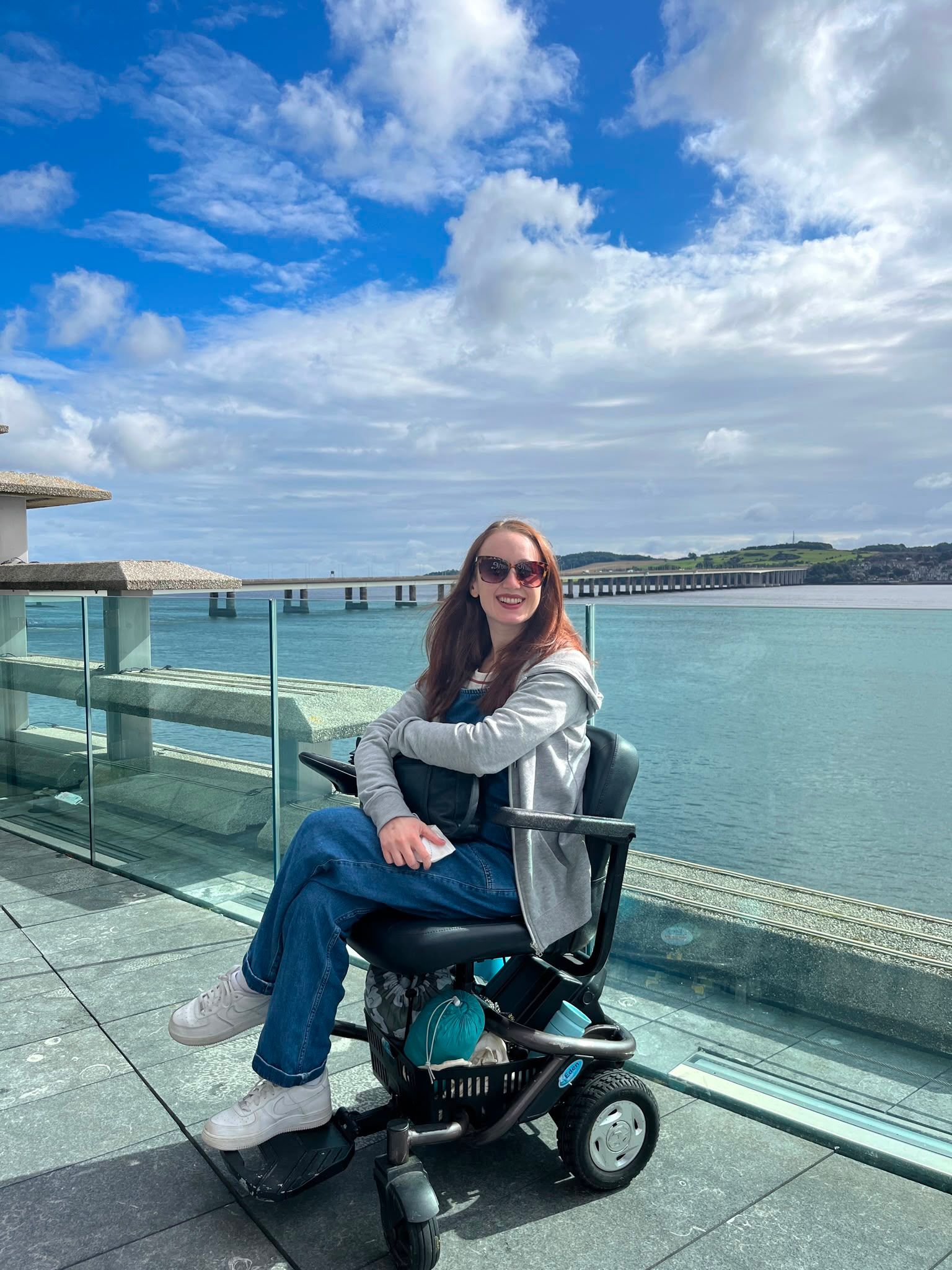 Pippa in her Powerchair with the sea behind her. 