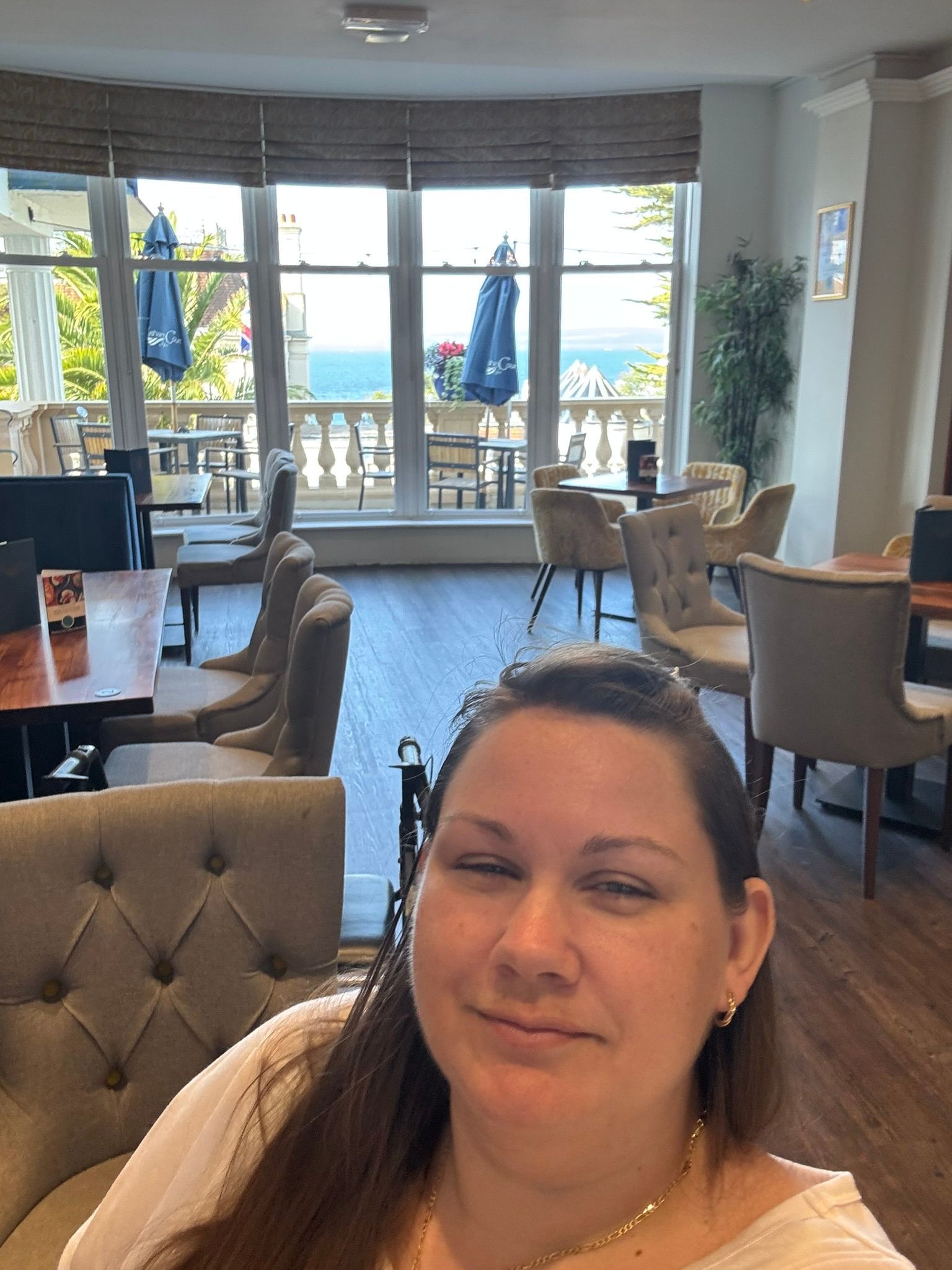 Victoria sits in a big room, with table and chairs and a big bay window at the end overlooking trees and the sea. 