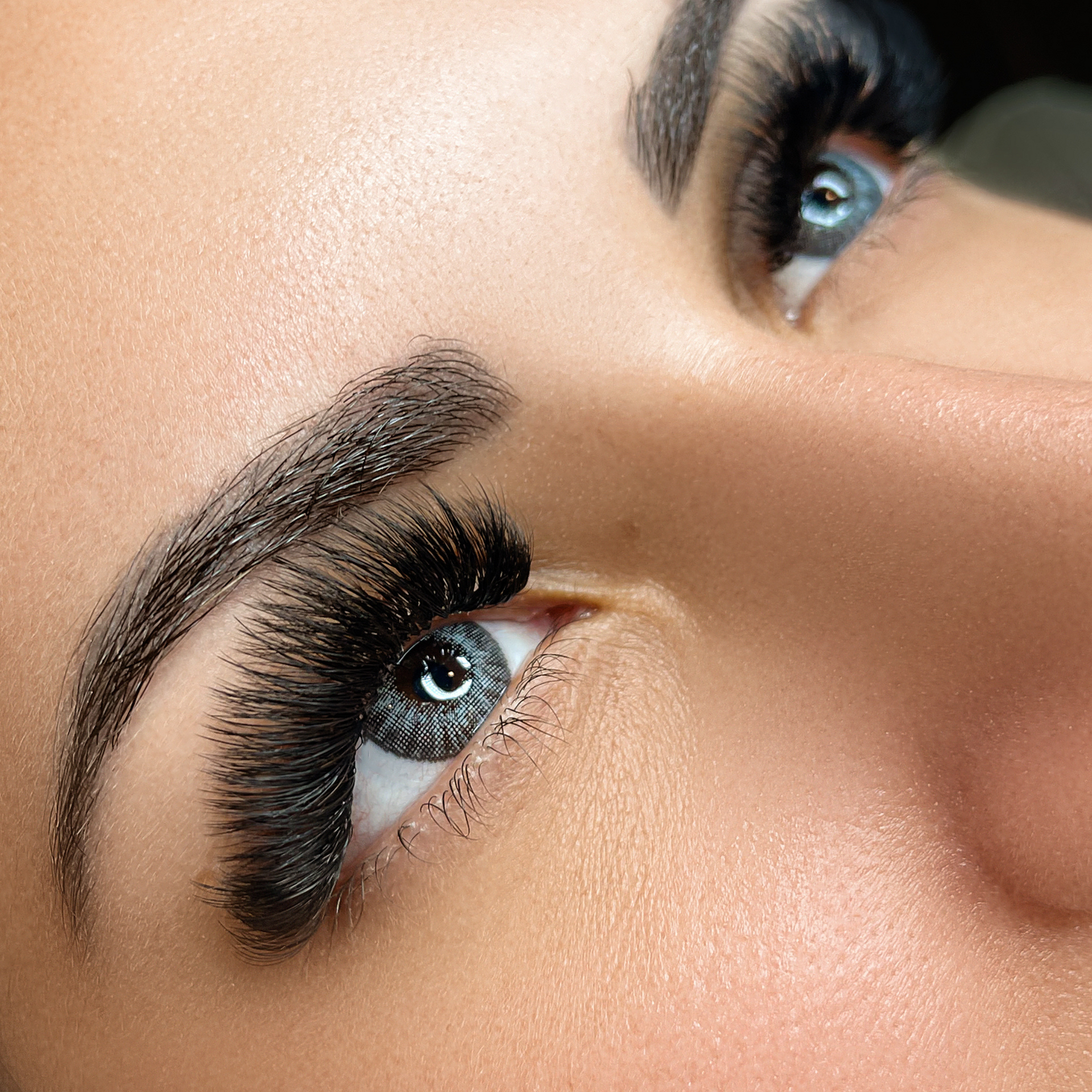 Close-up of a person's eye with voluminous black lash extensions, defined eyebrows, and bright blue eyes.