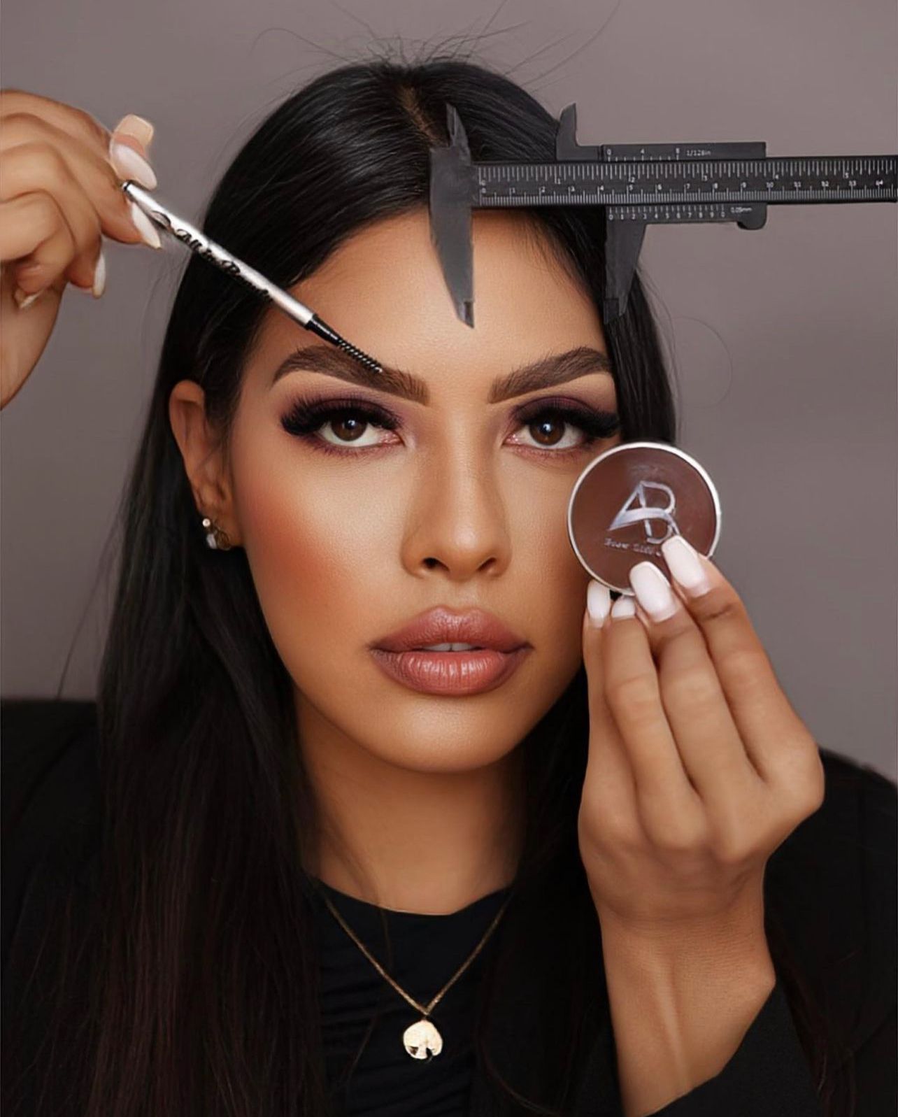 Woman shaping eyebrow with makeup tools, holding brow product.