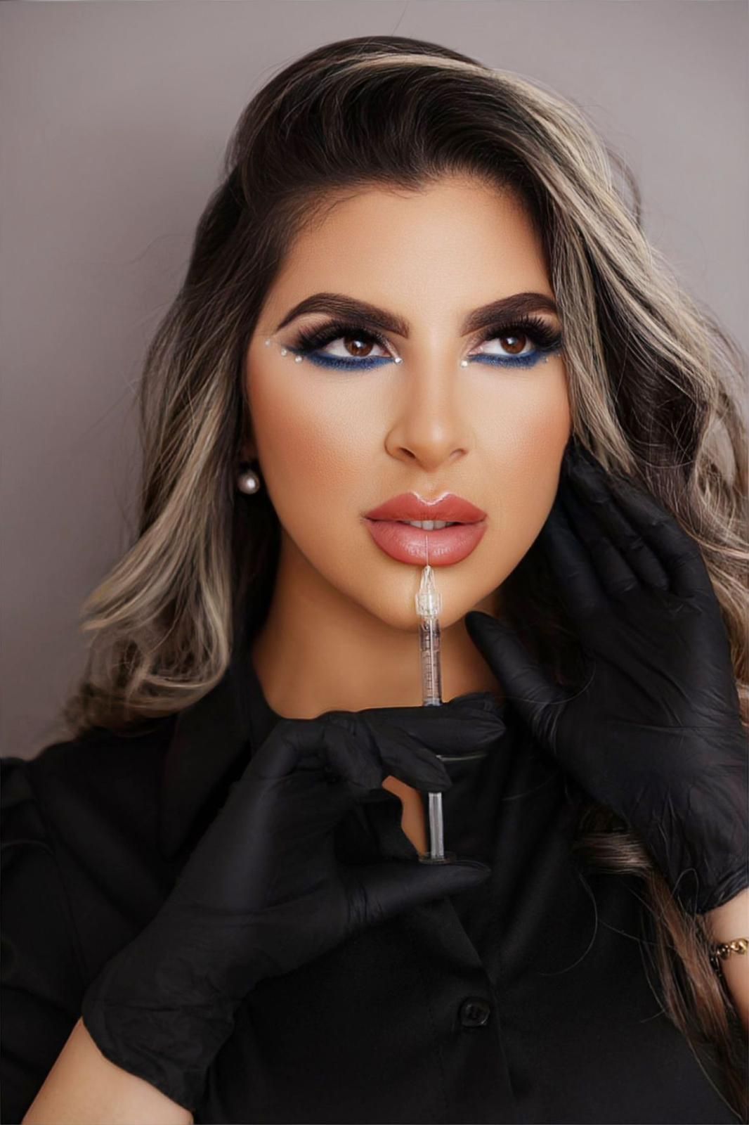 Woman holding a syringe near her lips; wearing gloves and dark makeup.