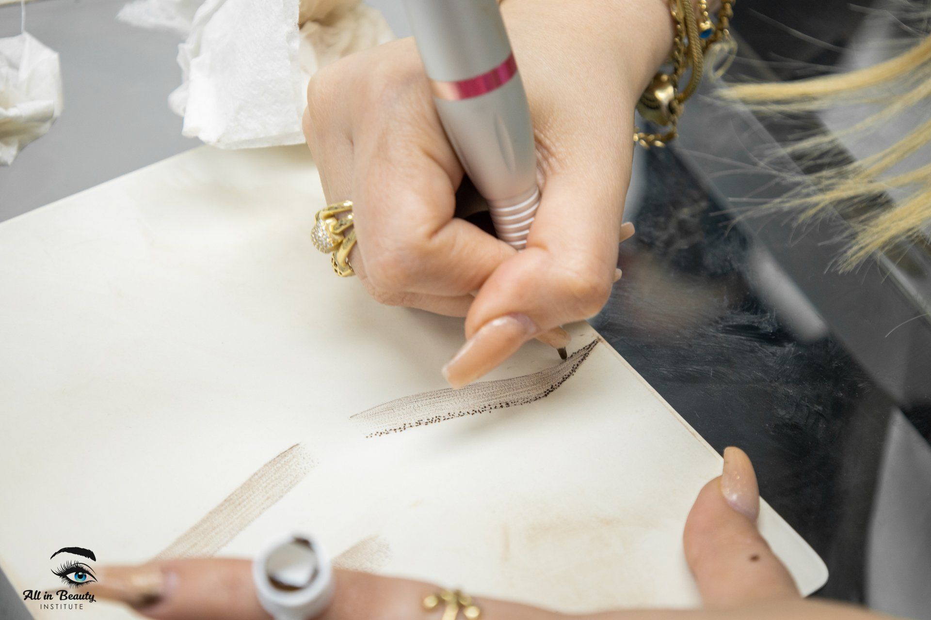 A person's hand using a tattoo pen, drawing on a practice pad.