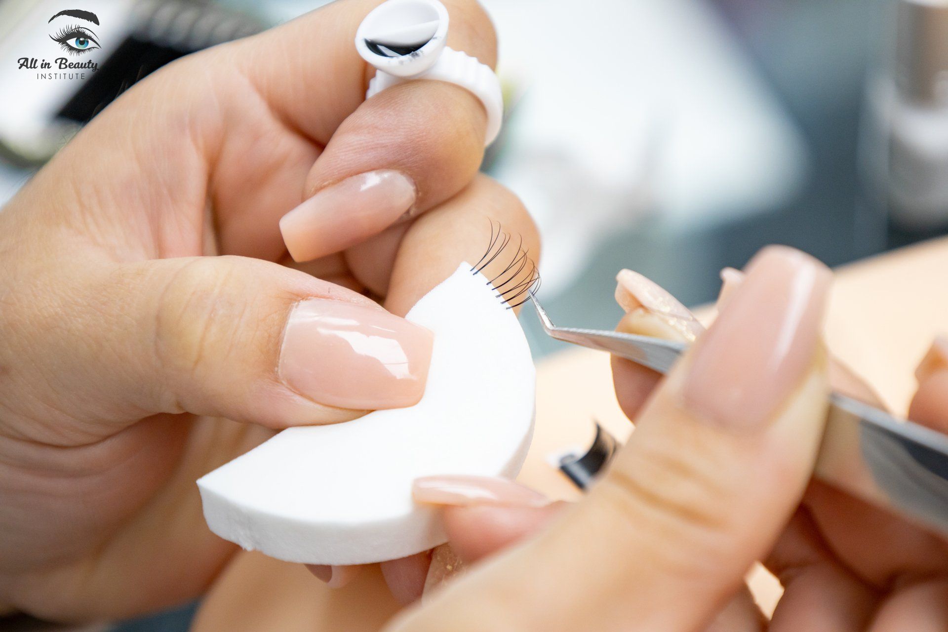Lash technician applying eyelash extensions with tweezers and a white applicator; close-up view.