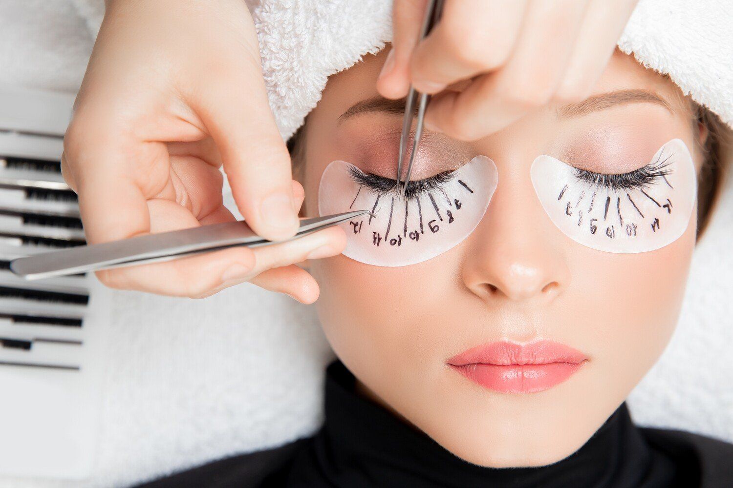 Woman getting eyelash extensions, hands using tweezers near eyes.