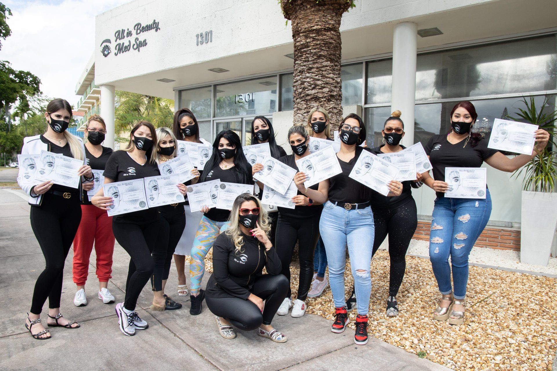 Group of women with certificates in front of a building; all wearing masks and black tops.