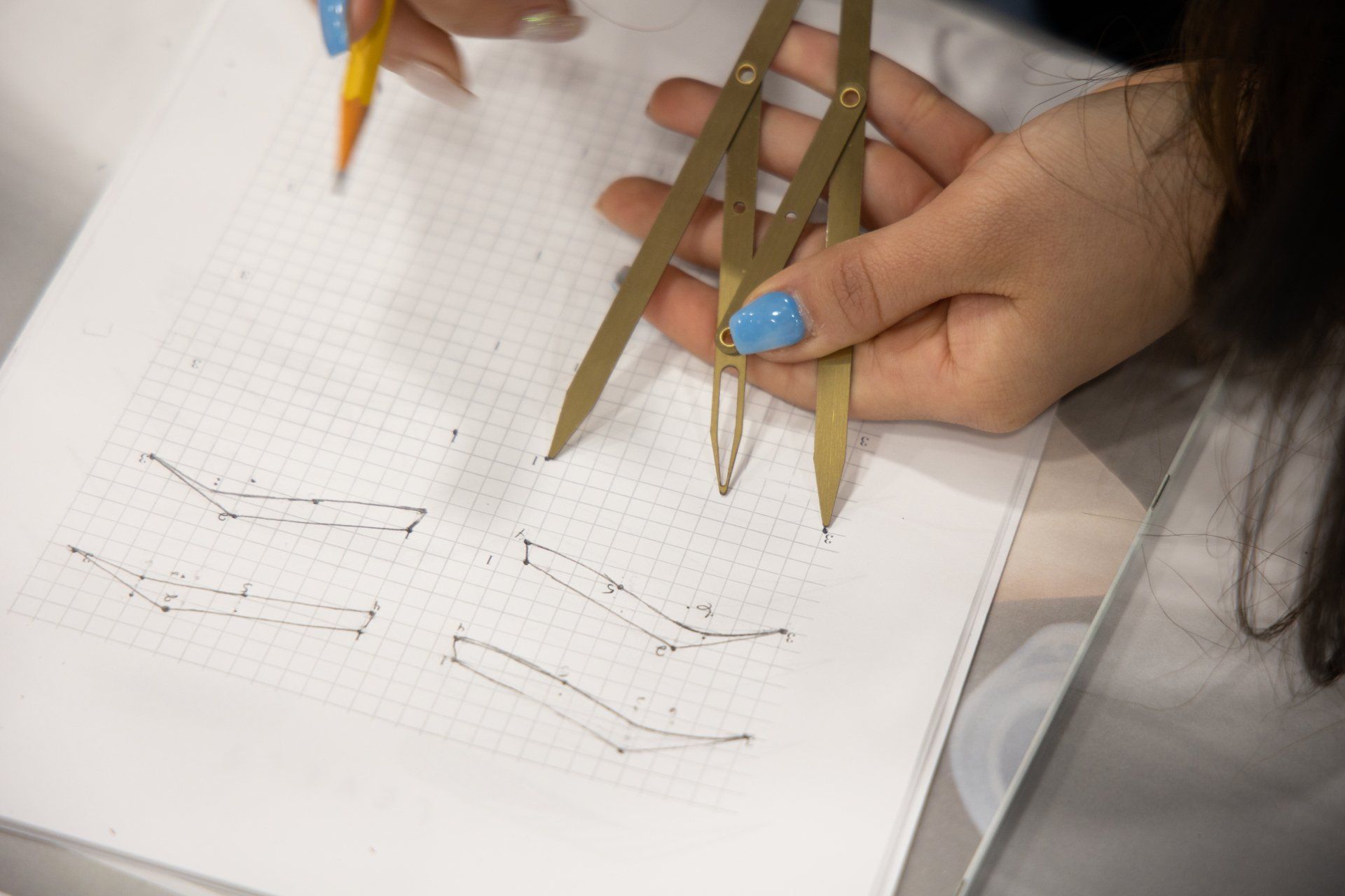 Person using dividers and pencil to draw on graph paper; examples of drawn shapes are visible.
