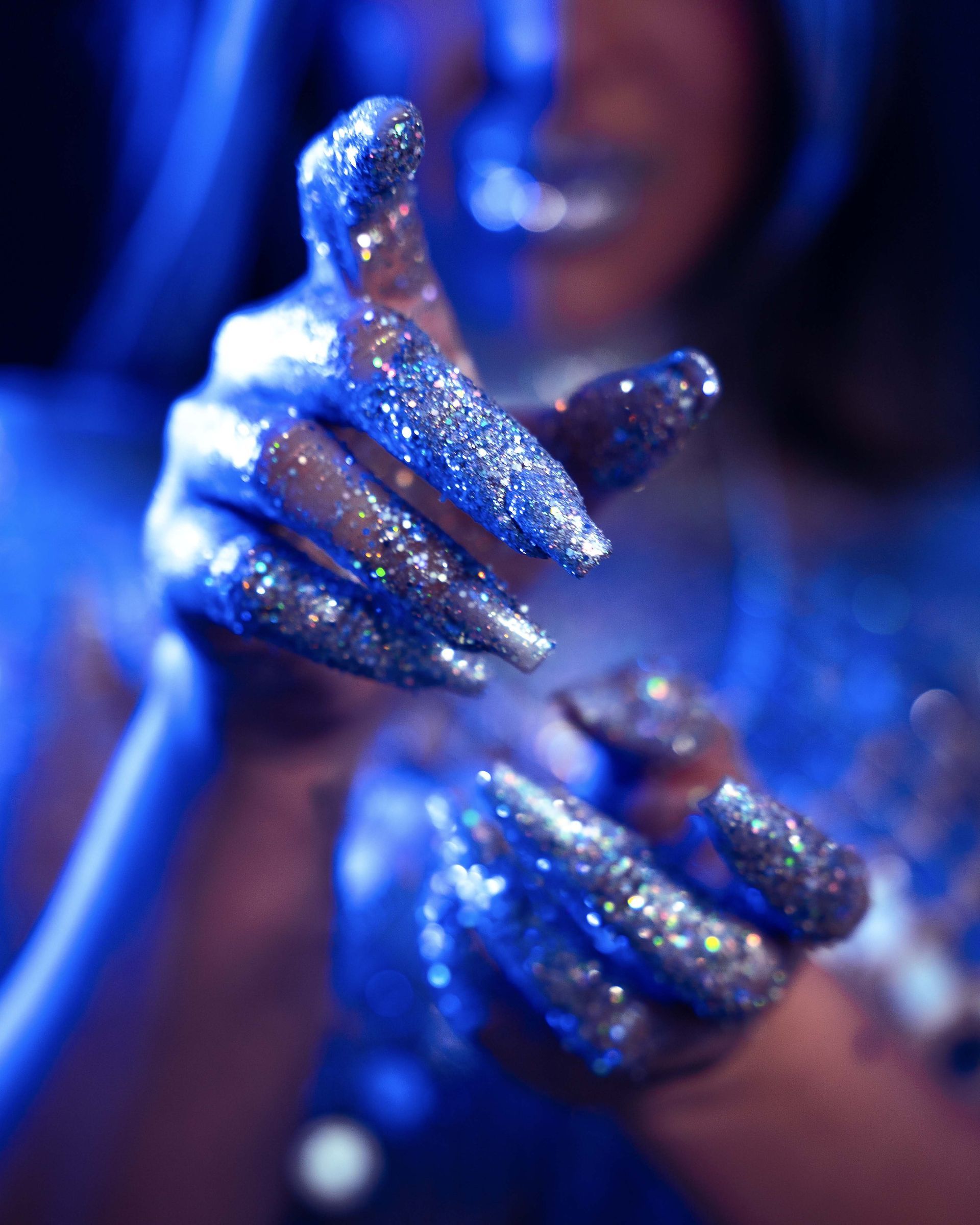 Hands covered in glitter, reaching forward with a blue hue.