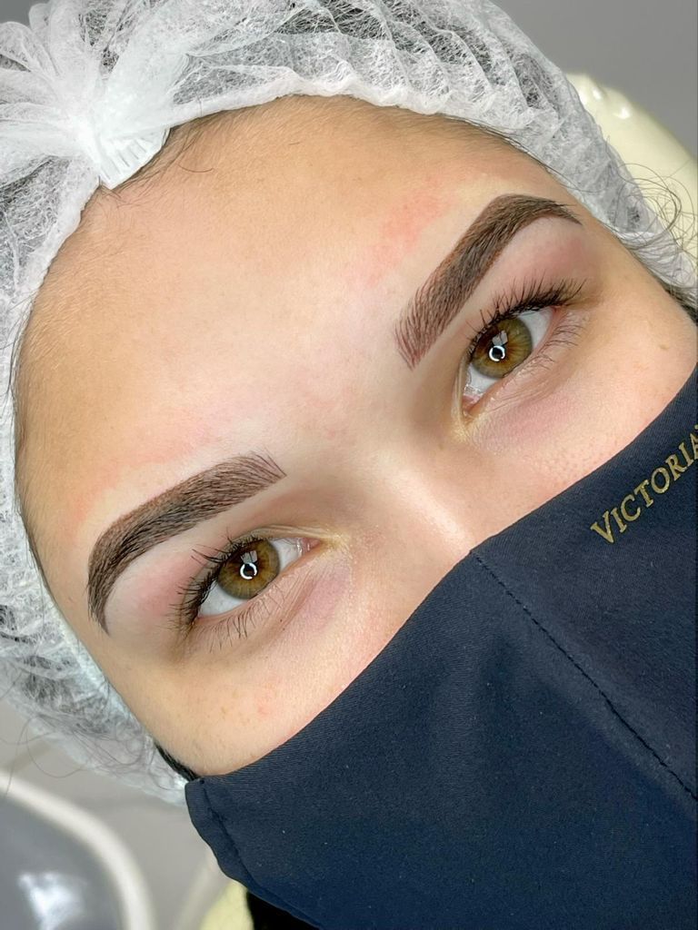 Woman with professionally styled brown eyebrows, wearing a mask and hairnet.